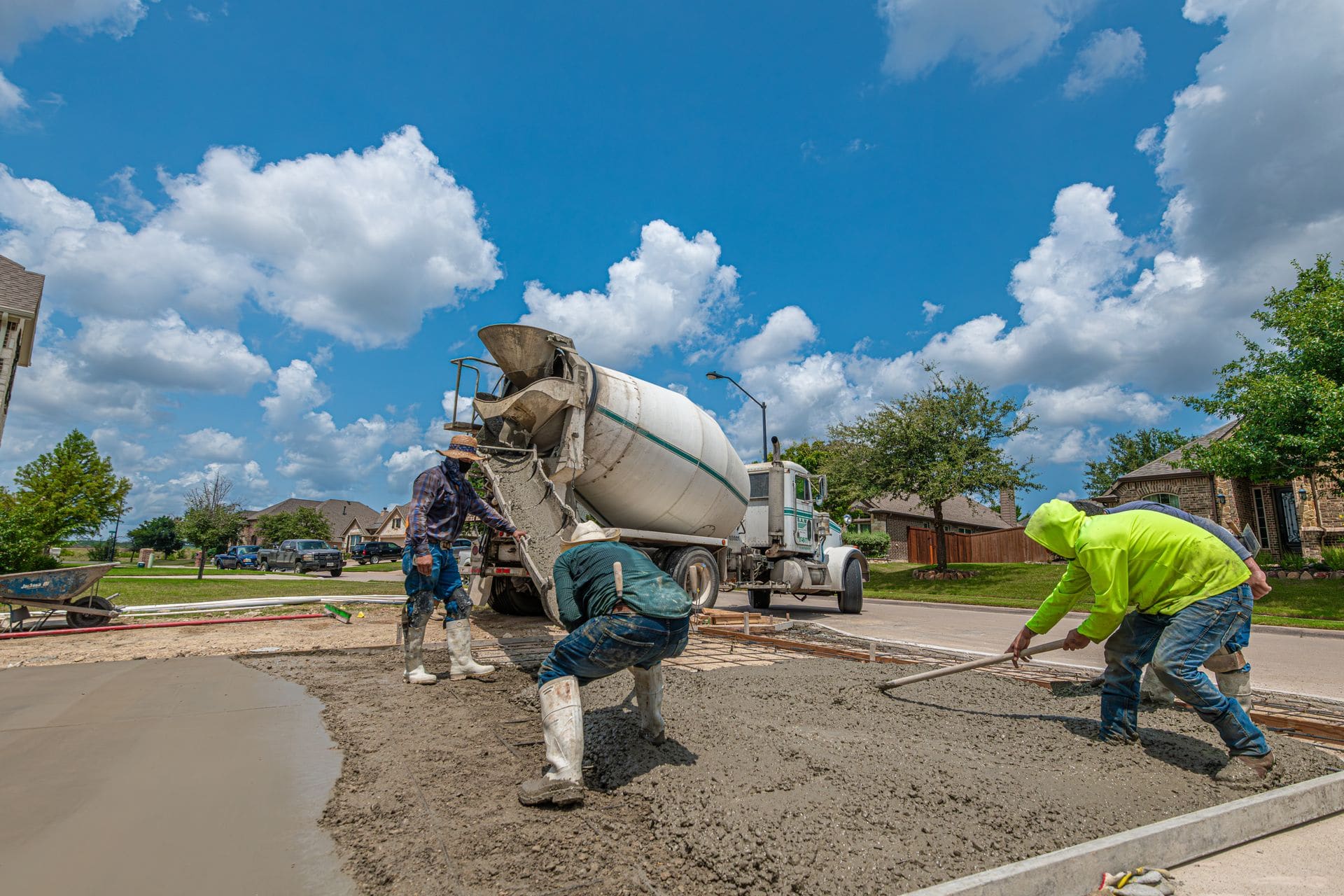 Concrete crew screeding a freshly poured residential driveway behind a mixer truck
